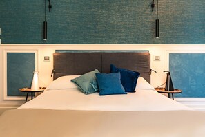 A large bed with a dark headboard, two bedside tables with lamps, and a teal textured wall. - AD MAIORA Boutique Suite (Naples)