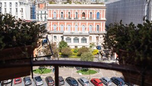 A view from a balcony overlooking a parking lot with several cars, a building with red and white facade, and a cityscape in the background. - AD MAIORA Boutique Suite (Naples)