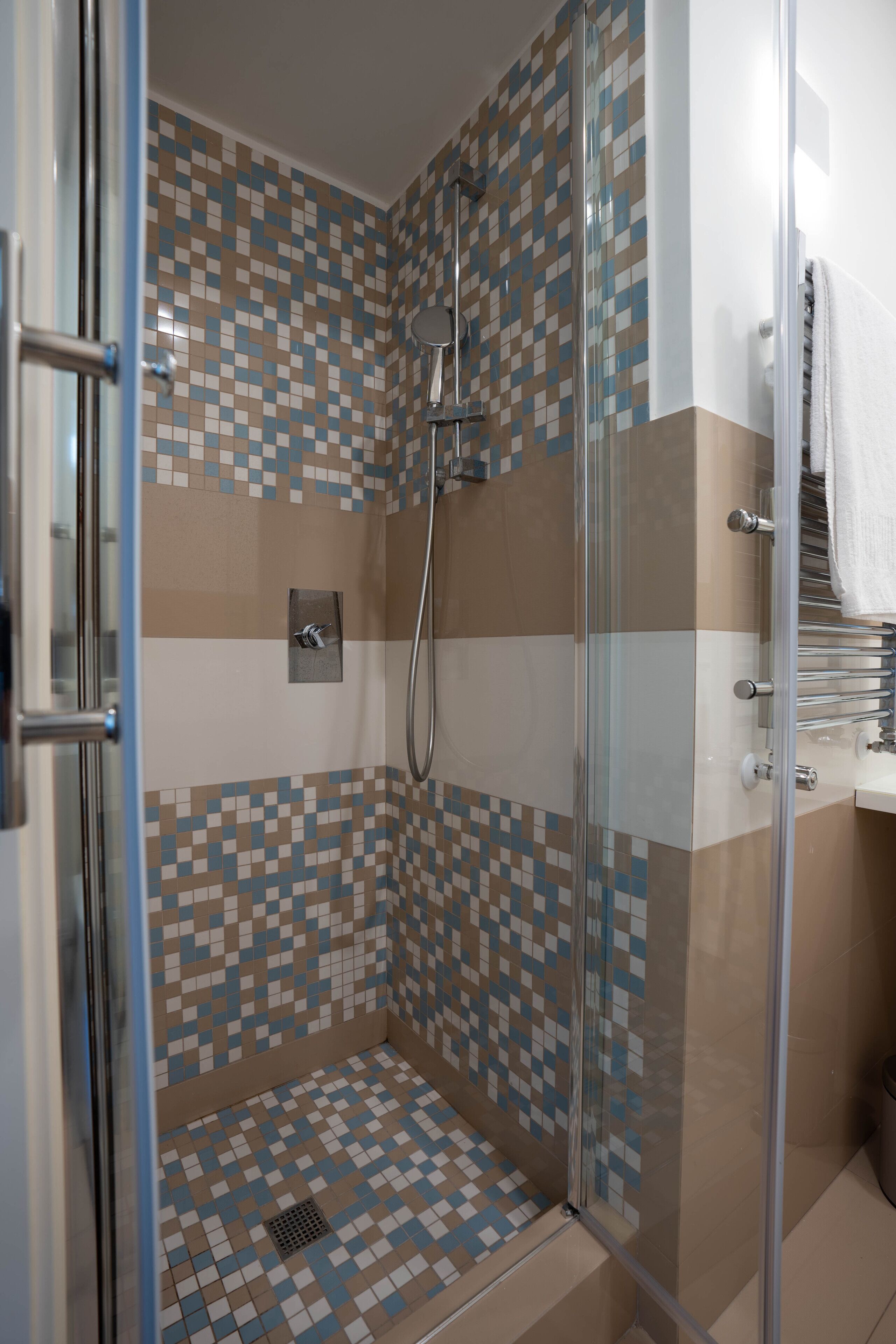 A glass-enclosed shower with a tiled floor and walls, a showerhead, and a towel rack.