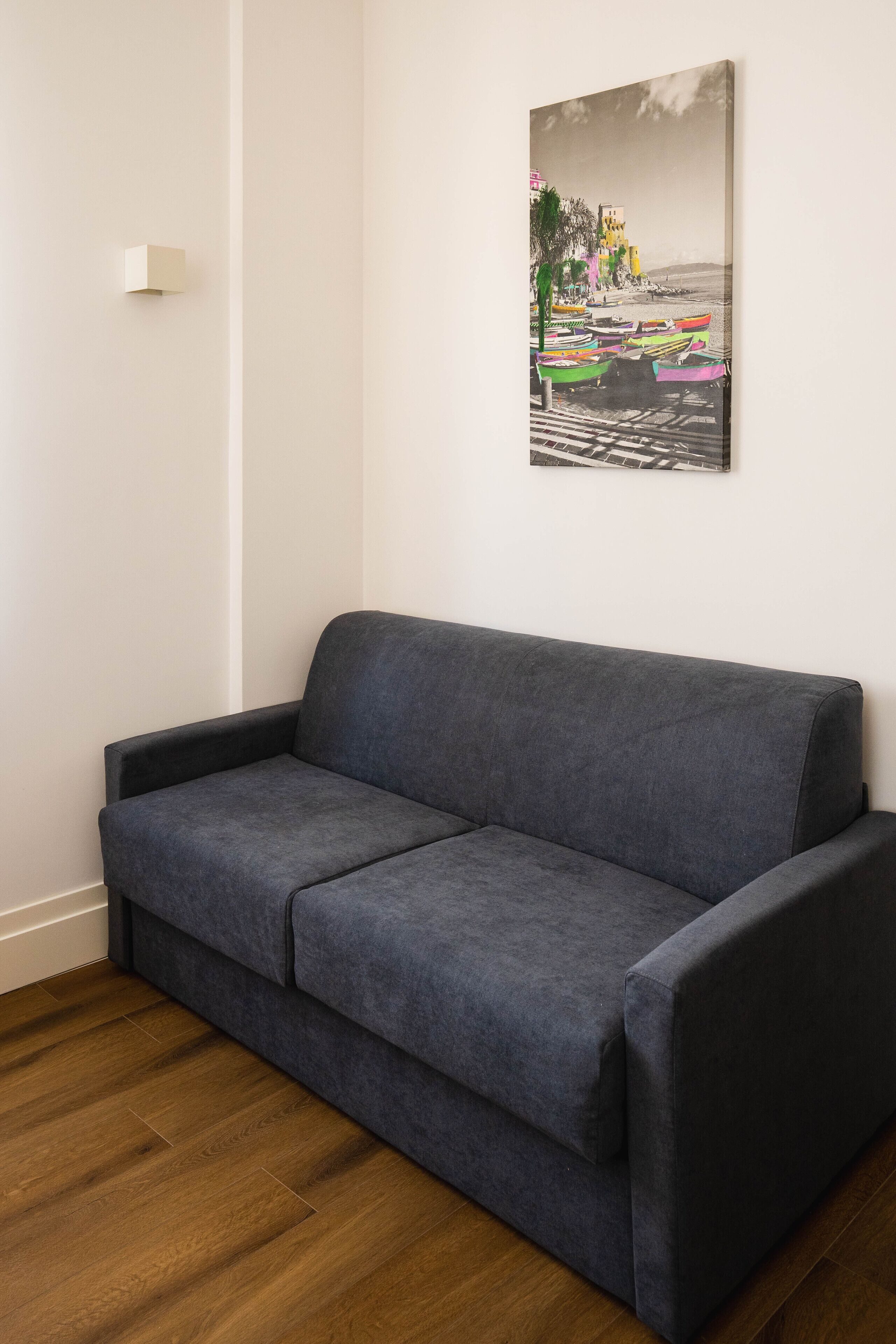A grey sofa against a white wall with a framed picture of boats and buildings.