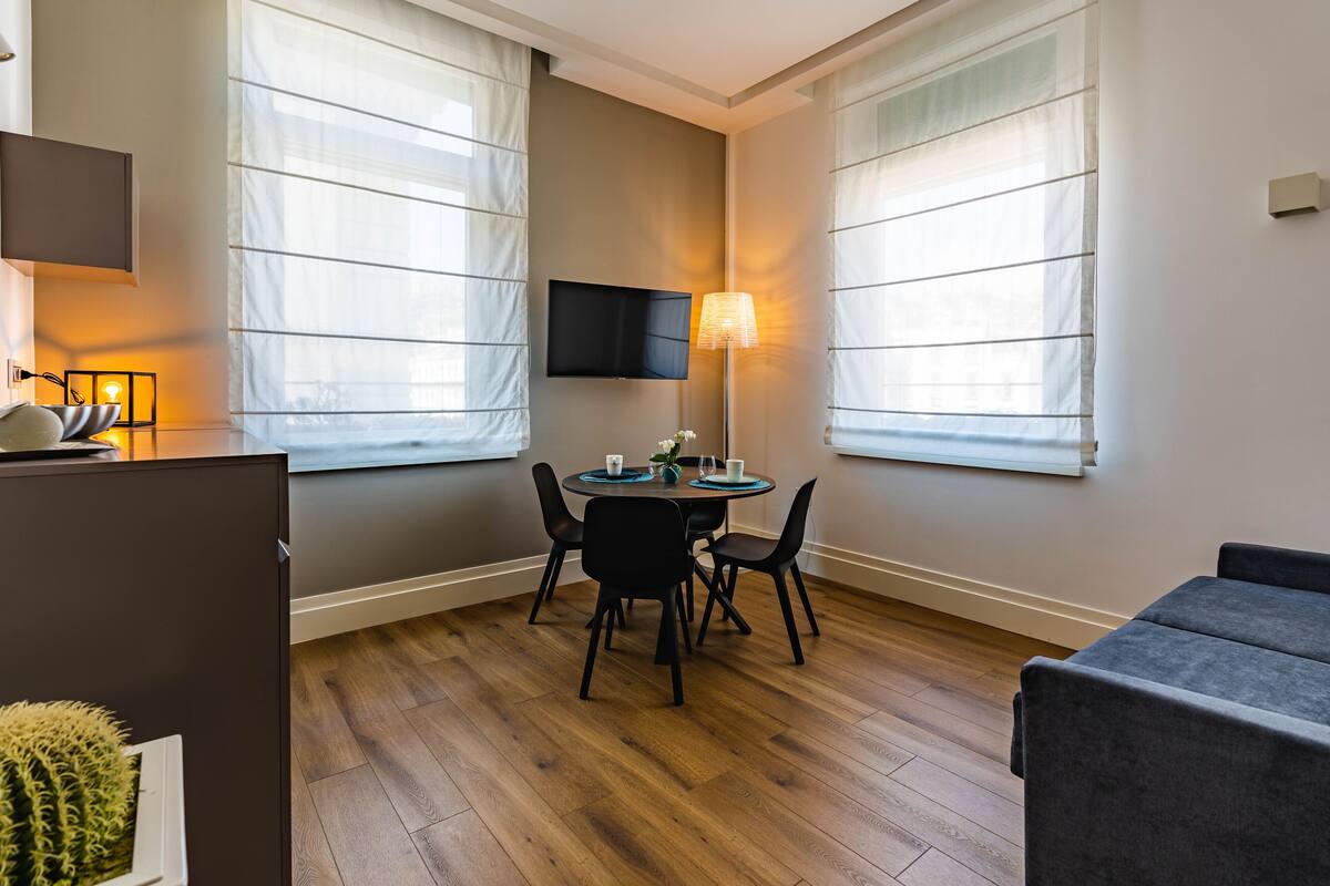 A modern room with a dining table, chairs, a flat-screen TV, and a sofa.