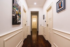 A hallway with white walls, dark wooden flooring, and doors leading to rooms. There are artworks on the walls. - AD MAIORA Boutique Suite (Naples)