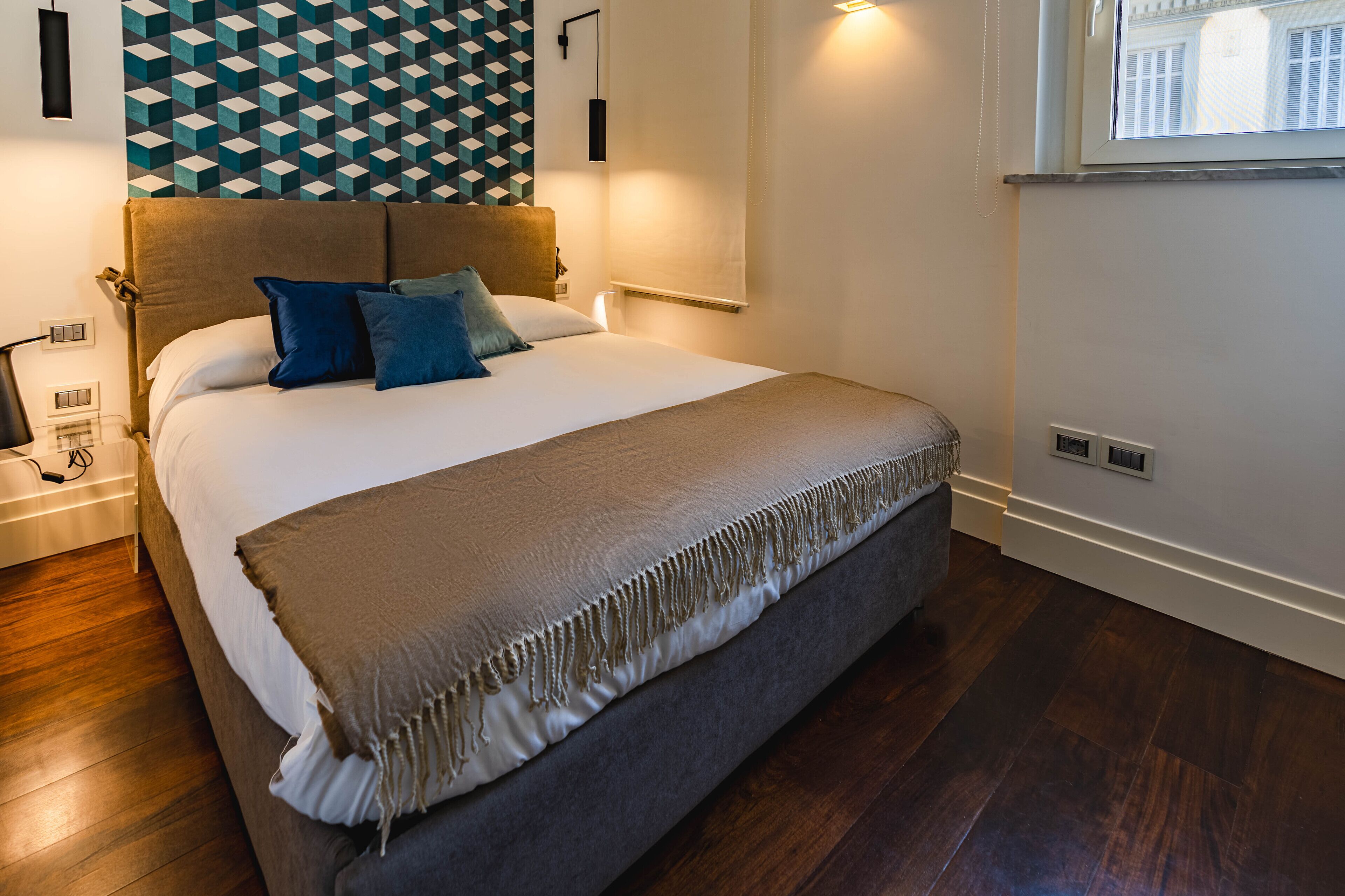 A modern bedroom with a large bed, a geometric patterned wall, and a window with blinds.