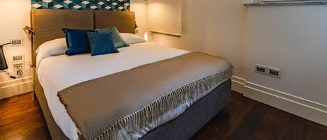 A modern bedroom with a large bed, a geometric patterned wall, and a window with blinds.