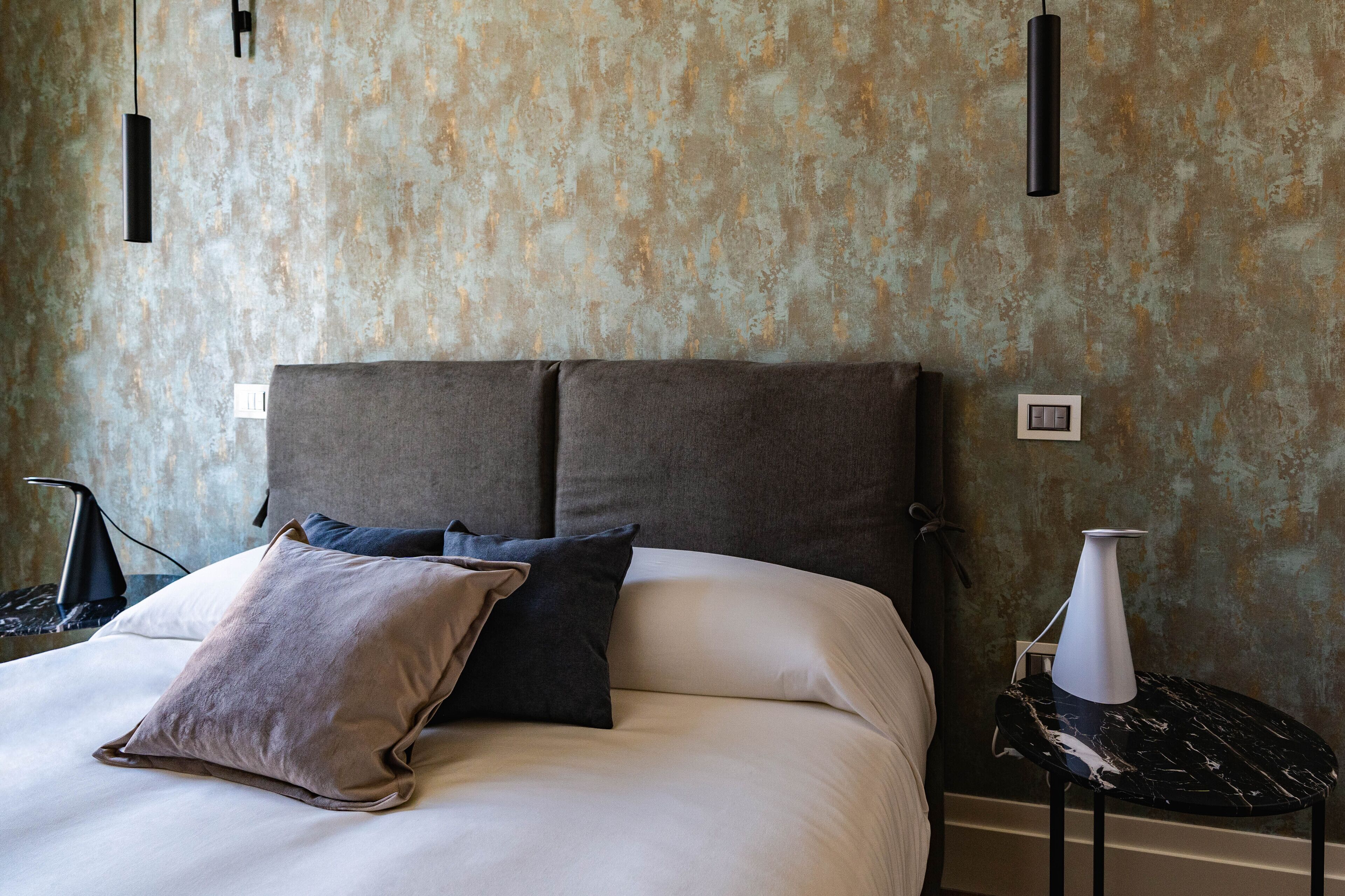 A modern bedroom with a large bed, a nightstand, and a wall-mounted lamp.