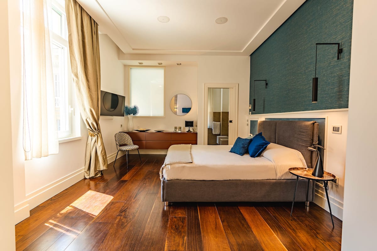 A modern bedroom with a large bed, a desk, a chair, and a TV.