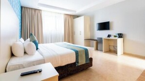 Habitación de hotel moderna con cama, escritorio, televisión y ventana con cortinas.