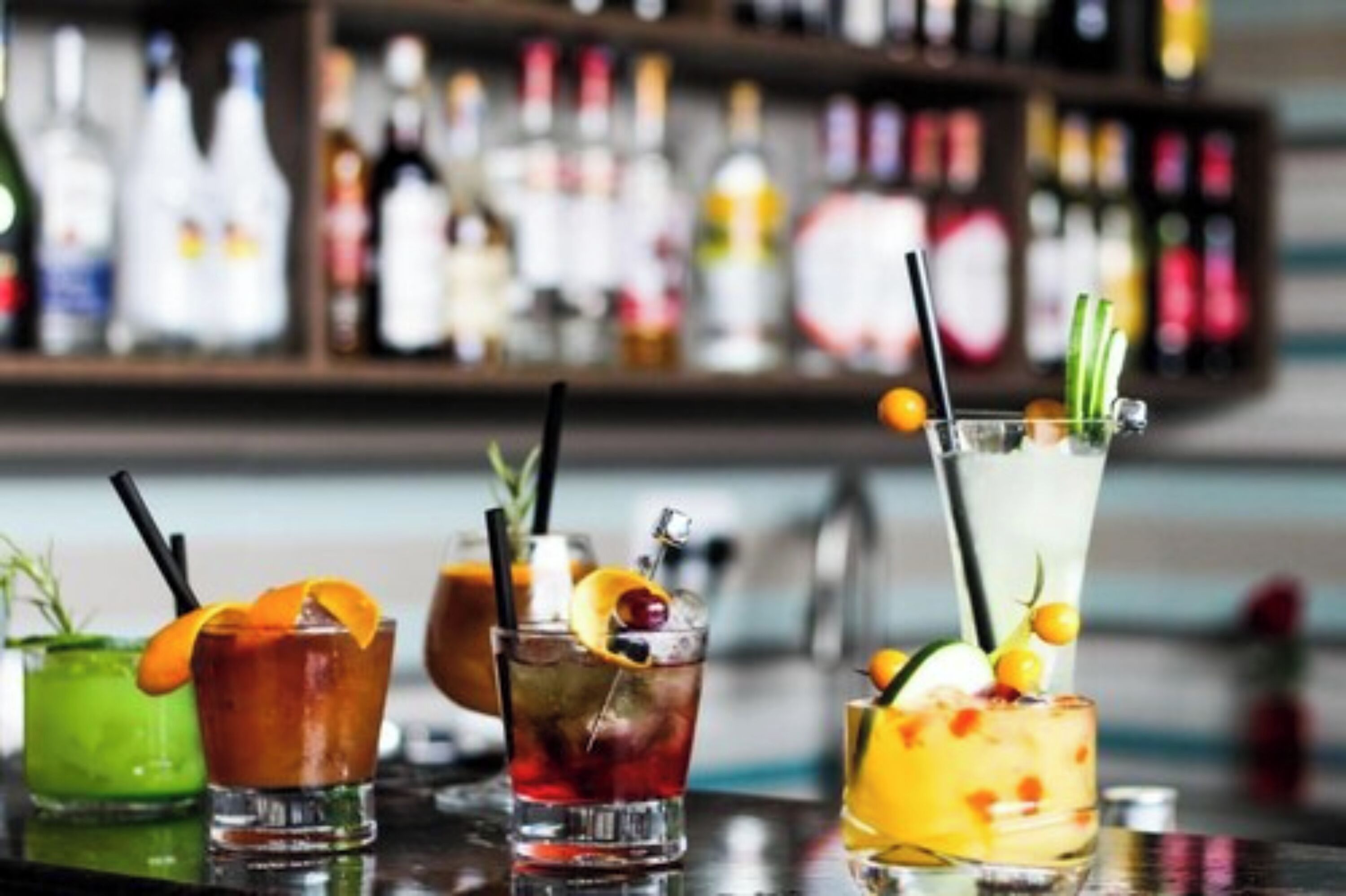 A bar with various drinks, including cocktails with garnishes and a green cocktail.