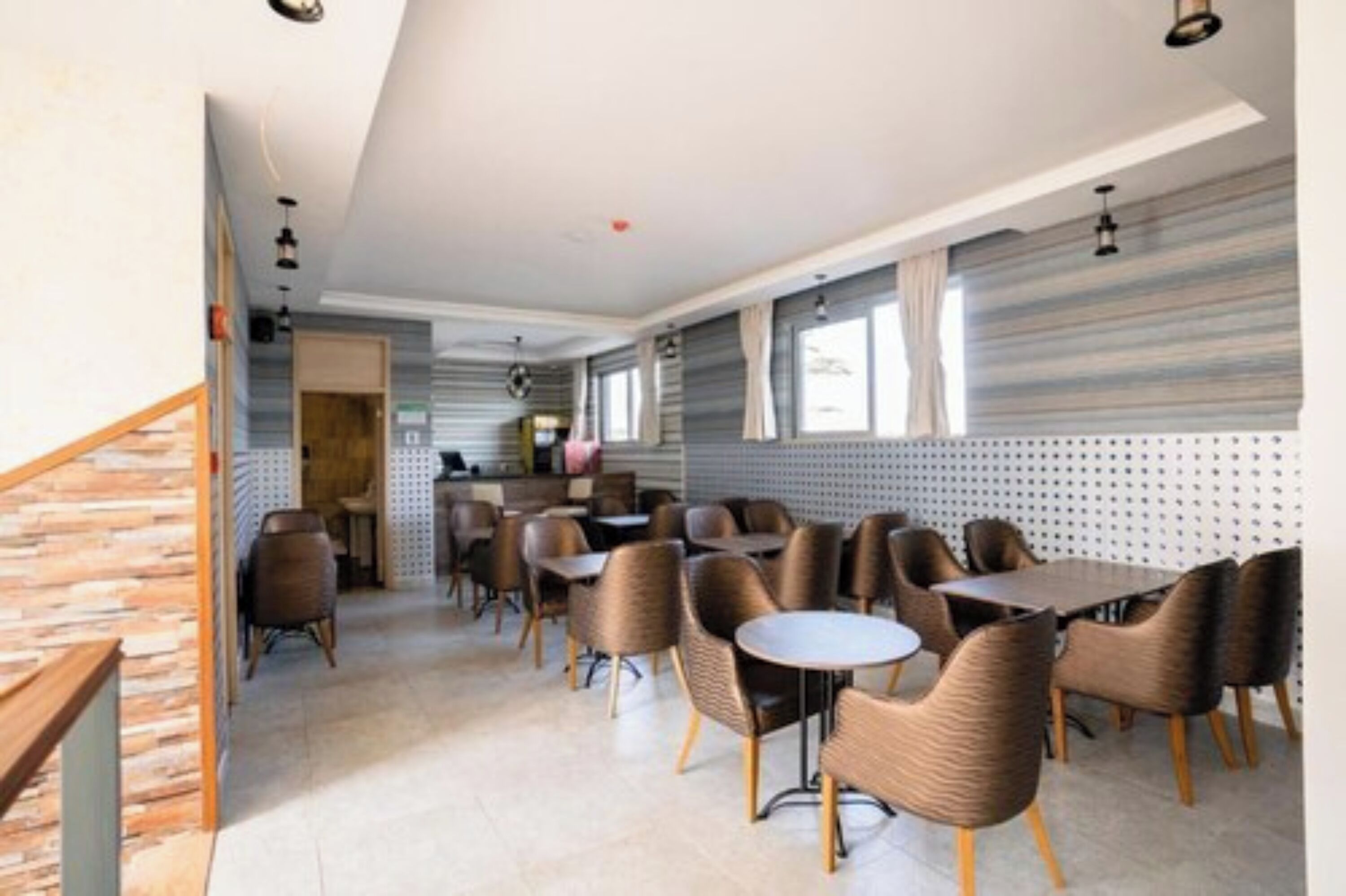 A modern dining area with multiple tables and chairs, a kitchen in the background, and a staircase on the left.