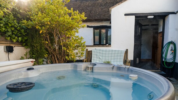 Een bubbelbad in een tuin, met een gebouw met rieten dak op de achtergrond.
