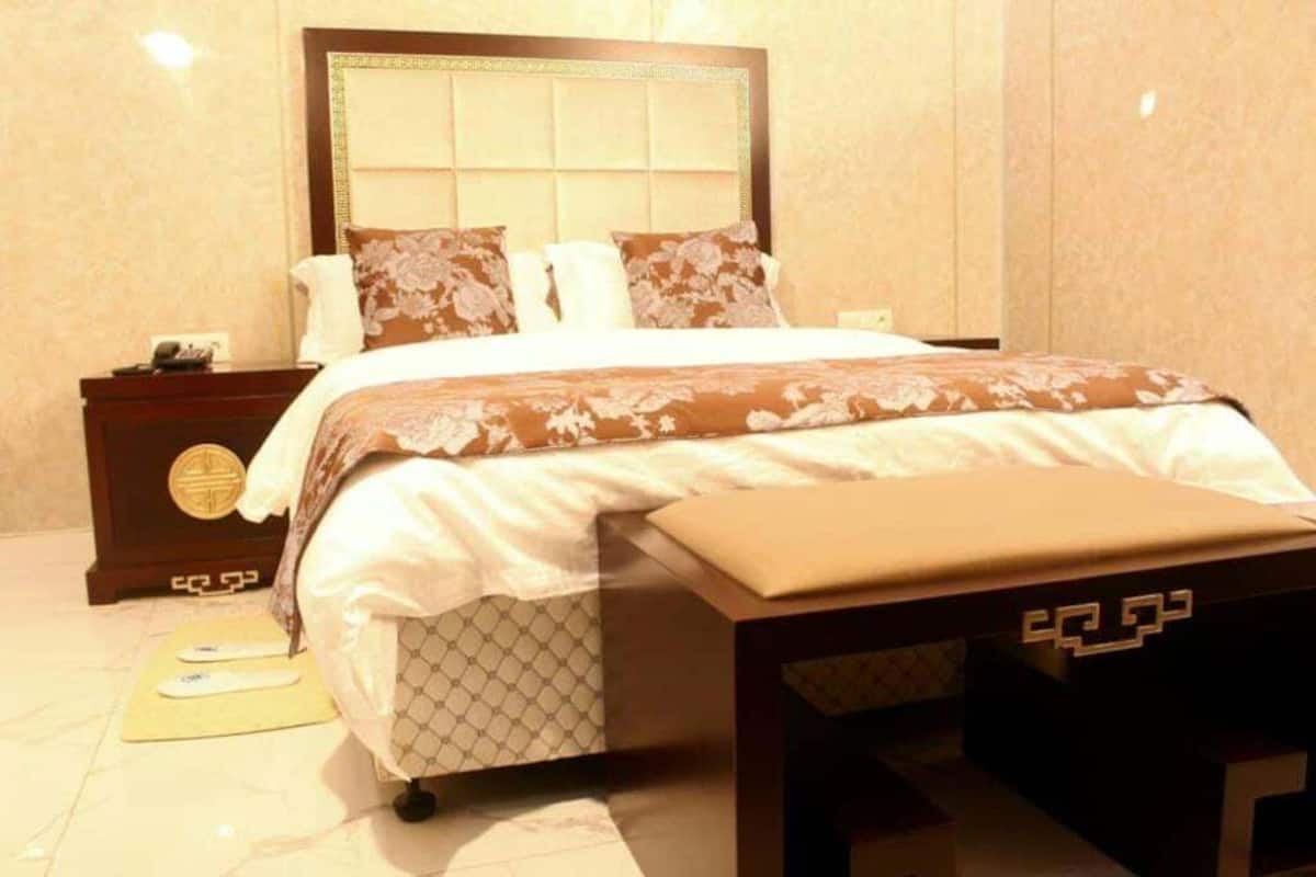 Una habitación de hotel con una cama grande, una mesita de noche, un banco y un reloj fijado a la pared.