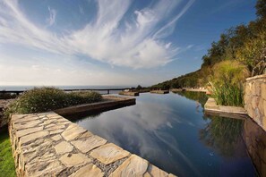 Une piscine à débordement aux bords en pierre, offrant une vue dégagée sur l’horizon.