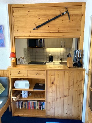 A compact kitchen with wooden cabinetry, a microwave, a coffee maker, and various utensils.