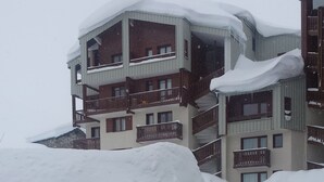 Un'auto ricoperta di neve parcheggiata di fronte a un edificio con diversi balconi e una montagna di neve.