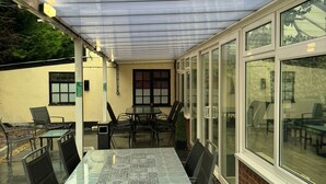 Une terrasse extérieure avec une table et des chaises en verre, un espace salon couvert et un mur en briques.