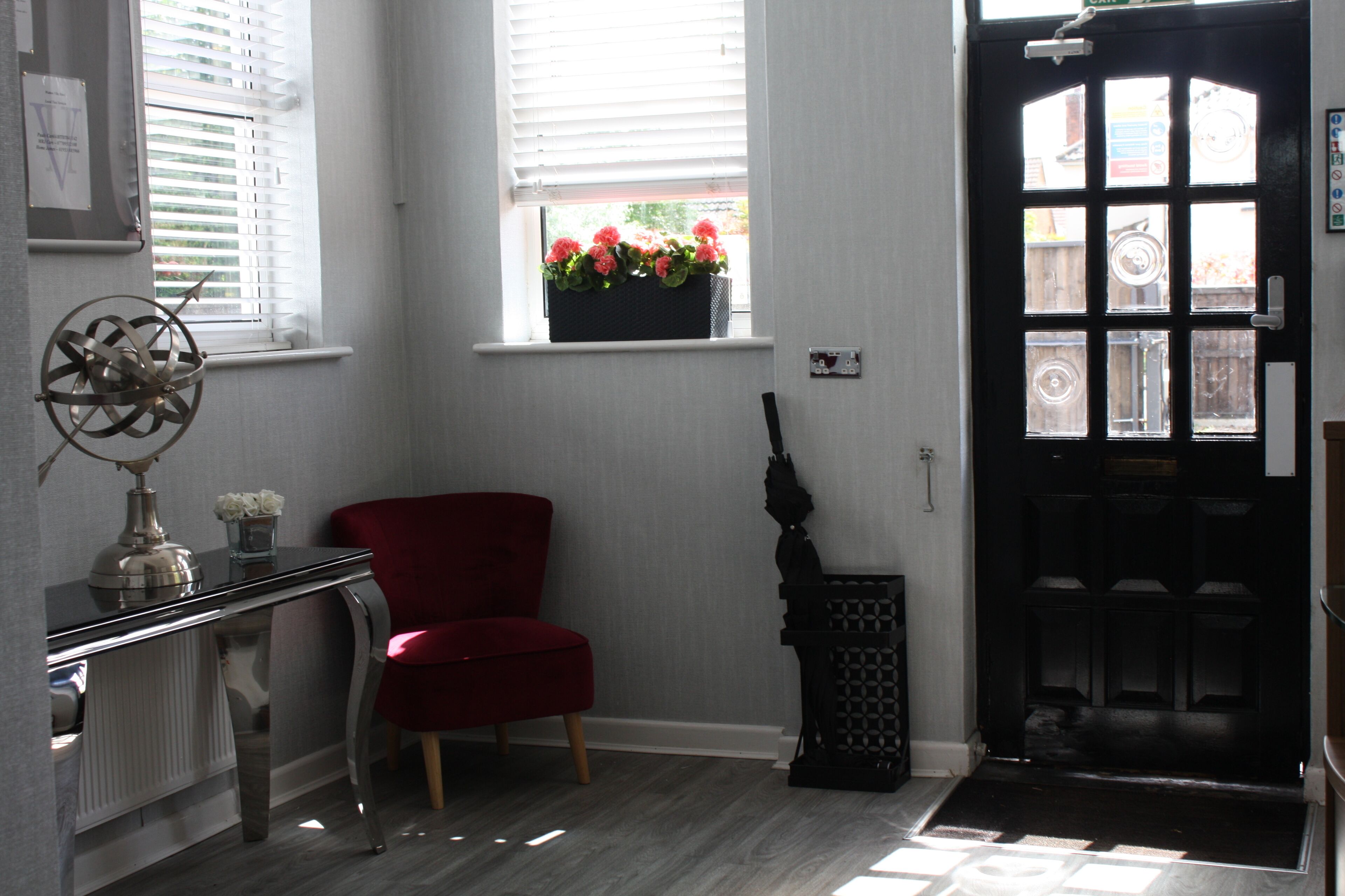 Une pièce avec une chaise rouge, une porte noire, une fenêtre avec un jardon et un radiateur.