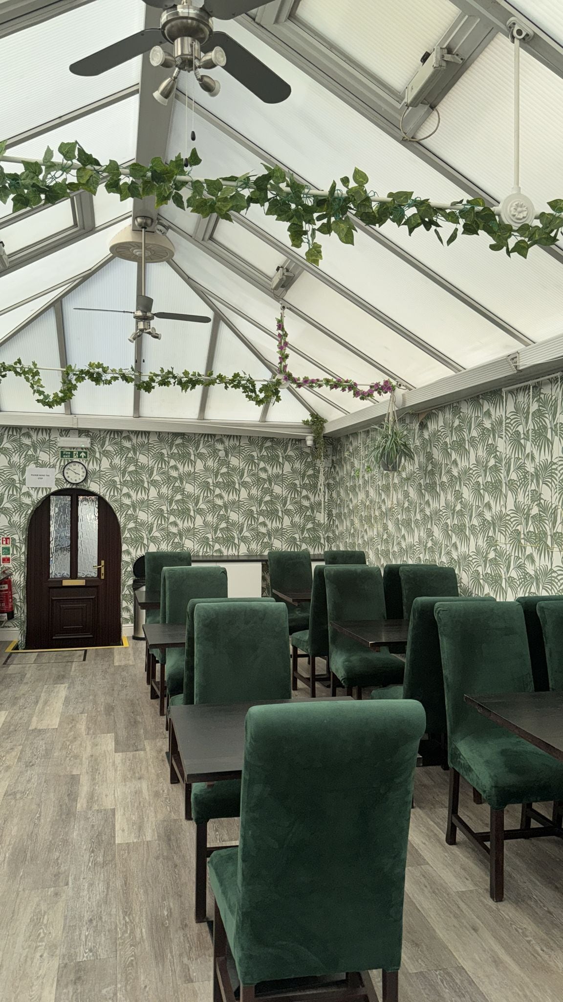 A greenhouse-style room with a high ceiling, green chairs, and a wooden door.