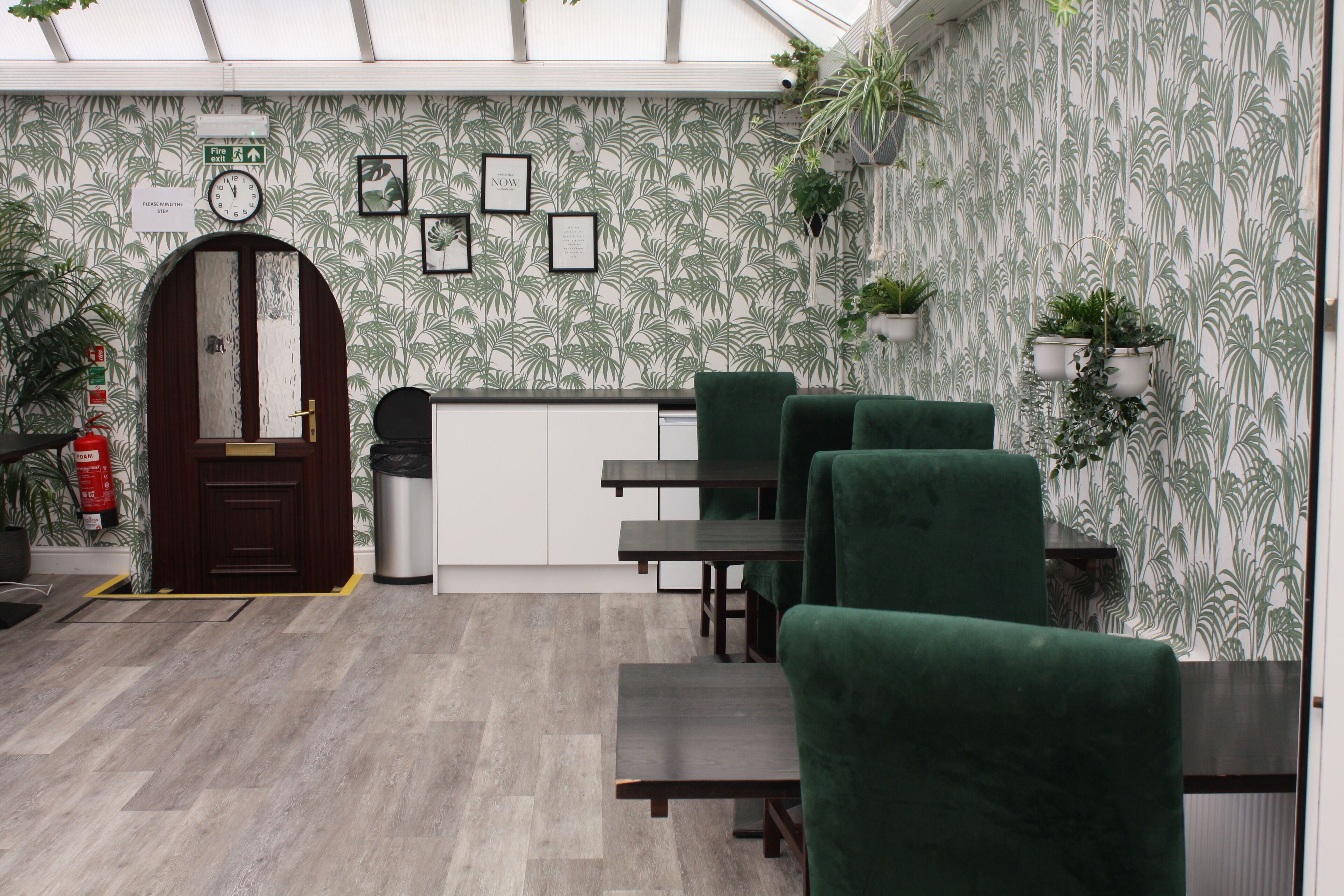 Un ristorante con sedie rivestite di verde, una porta in legno e carta da parati decorata.