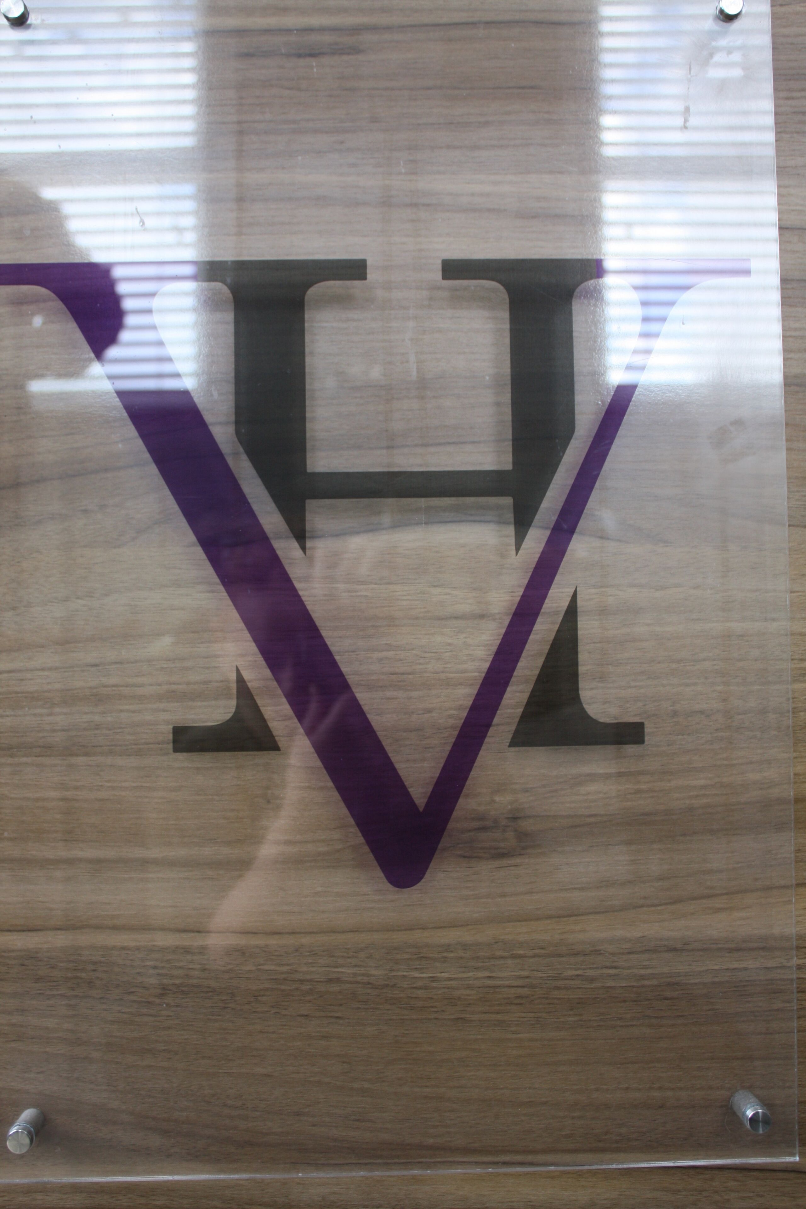 A wooden sign with a large, stylized letter "V" and a smaller "H" above it, mounted on a wall.