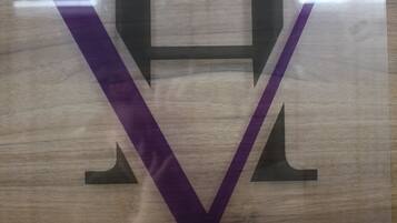 A wooden sign with a large, stylized letter "V" and a smaller "H" above it, mounted on a wall.