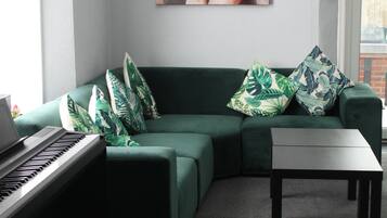 A modern living room with a green sofa, a piano, and a painting on the wall.