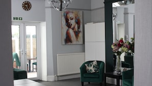 Un hall d’entrée avec des fauteuils verts, un tableau au mur, un vase de fleurs et une horloge.