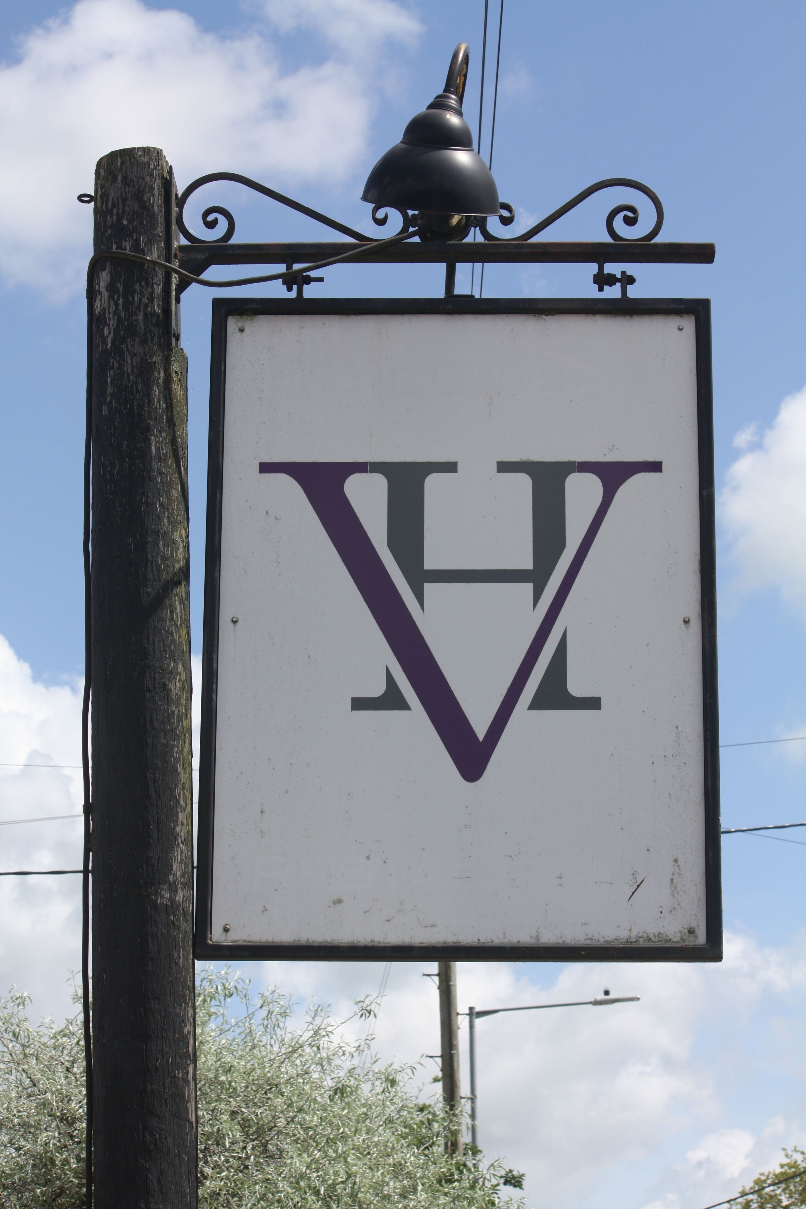 A sign with a large 'V' and 'H' in purple and black, mounted on a wooden post with a decorative metal fixture above it.