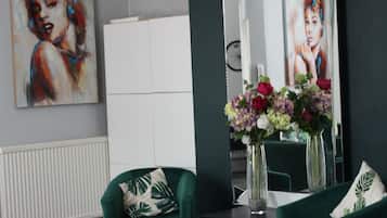 A modern living room with two green armchairs, a small table with a vase of flowers, a chandelier, and a large mirror reflecting the room.
