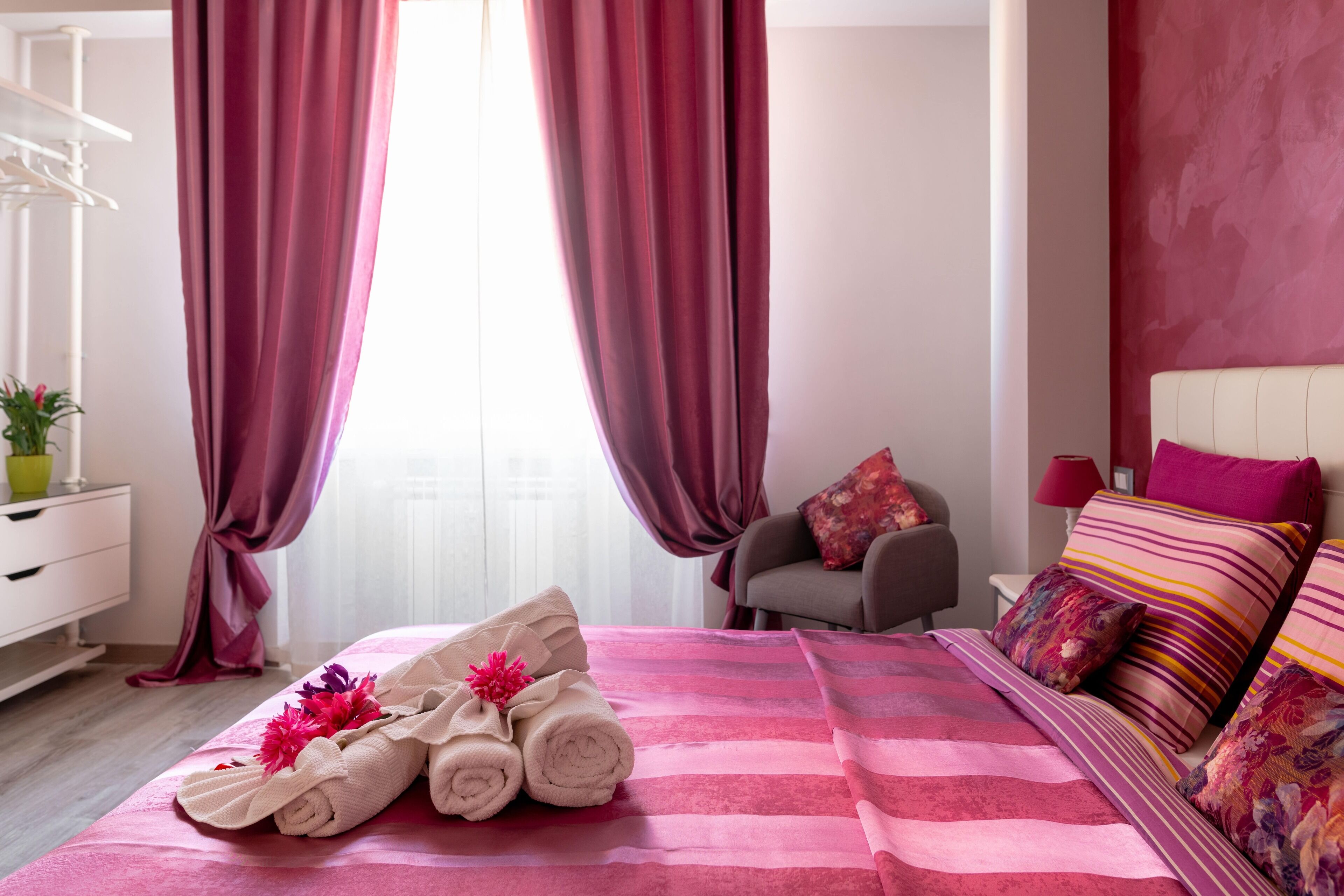 Hotellihuone, jossa on sänky, tuoli, yöpöytä ja ikkuna, jossa on verhot.