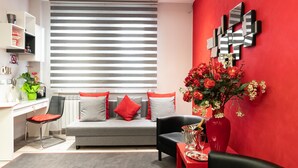 A modern living room with a grey sofa, red cushions, a black armchair, a red vase with flowers, and a red table with a champagne bottle. - B&B La Maison de Jo (Rome)