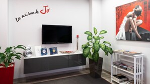 A modern living room with a flat-screen TV, a red potted plant, a white shelf with magazines, and a painting on the wall. - B&B La Maison de Jo (Rome)
