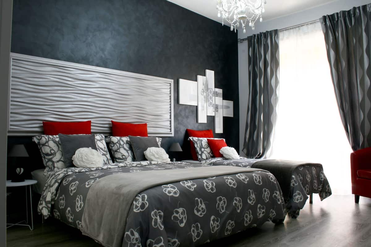 Quarto moderno com cama grande, mesa de cabeceira e uma cadeira vermelha.