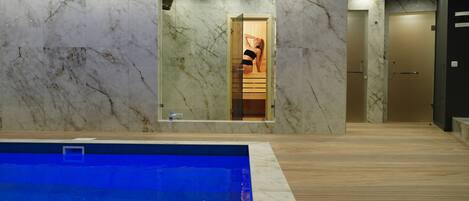 A modern indoor pool area with a marble wall and wooden flooring.