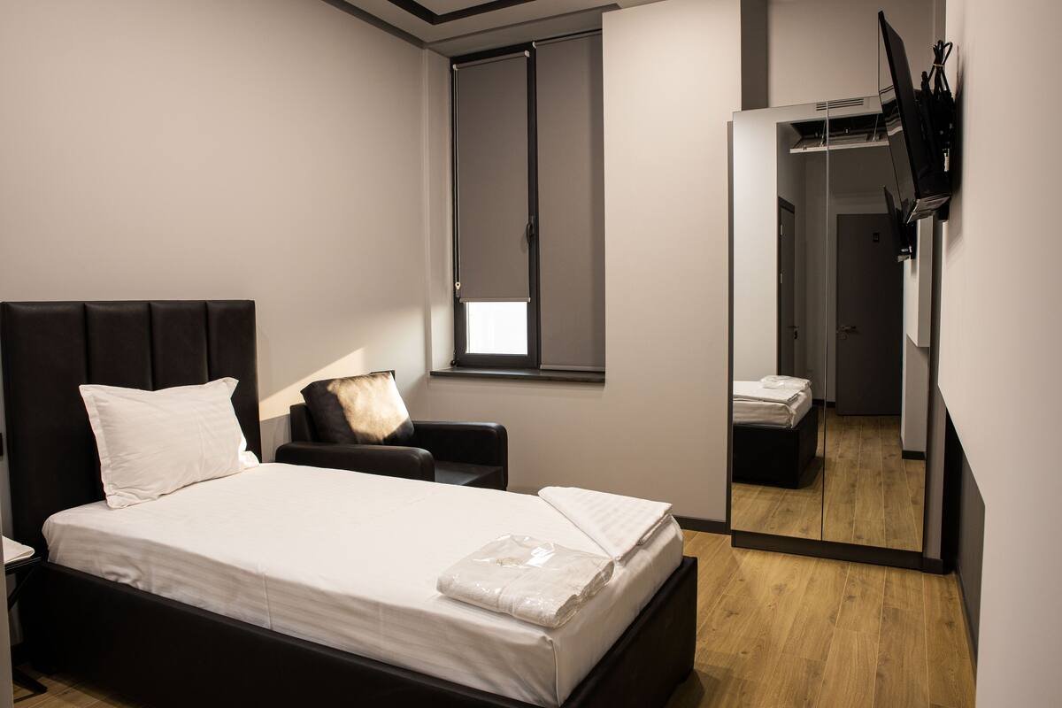 Ein modernes Hotelzimmer mit einem großen Bett, einer kleinen Sitzecke, einem Kleiderschrank und einem Spiegel, der das Zimmer reflektiert.