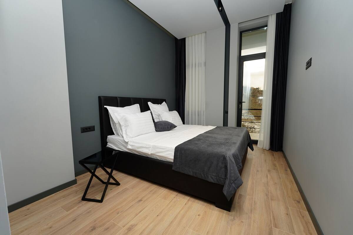 Ein modernes Schlafzimmer mit schwarzem Bettgestell, weißer Bettwäsche und einer grauen Tagesdecke.