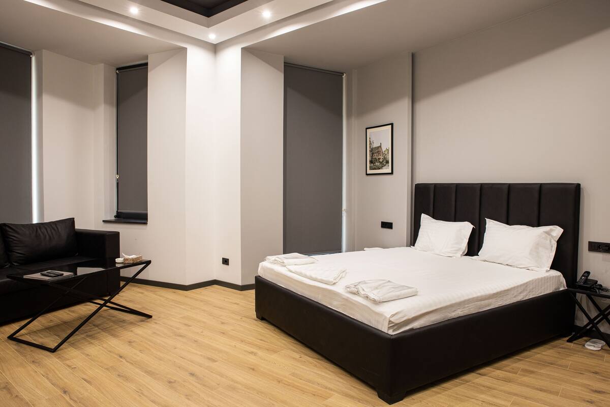 Ein modernes Schlafzimmer mit einem großen Bett, einer schwarzen Couch und einem Holzboden.