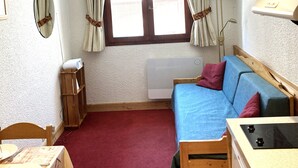 A cozy room with a wooden ceiling, a blue sofa, a wooden table with plates and cutlery, a window with curtains, and a hanging pot rack. - Tignes, Val Claret - at the centre of the Tignes and Val d'Isere ski area. (Tignes)