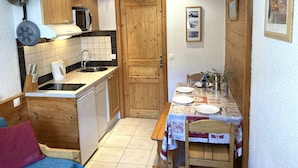 A compact kitchen with wooden cabinets, a sink, and a dining area with a table set for two. - Tignes, Val Claret - at the centre of the Tignes and Val d'Isere ski area. (Tignes)
