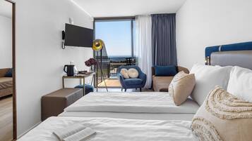 A modern hotel room with a large bed, a desk, a chair, a TV, and a balcony with a view.