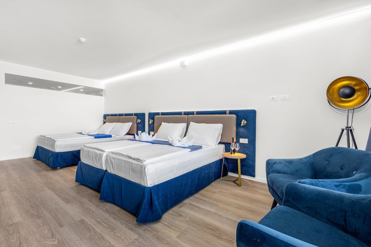 A modern hotel room with two beds, a blue armchair, and a floor lamp.