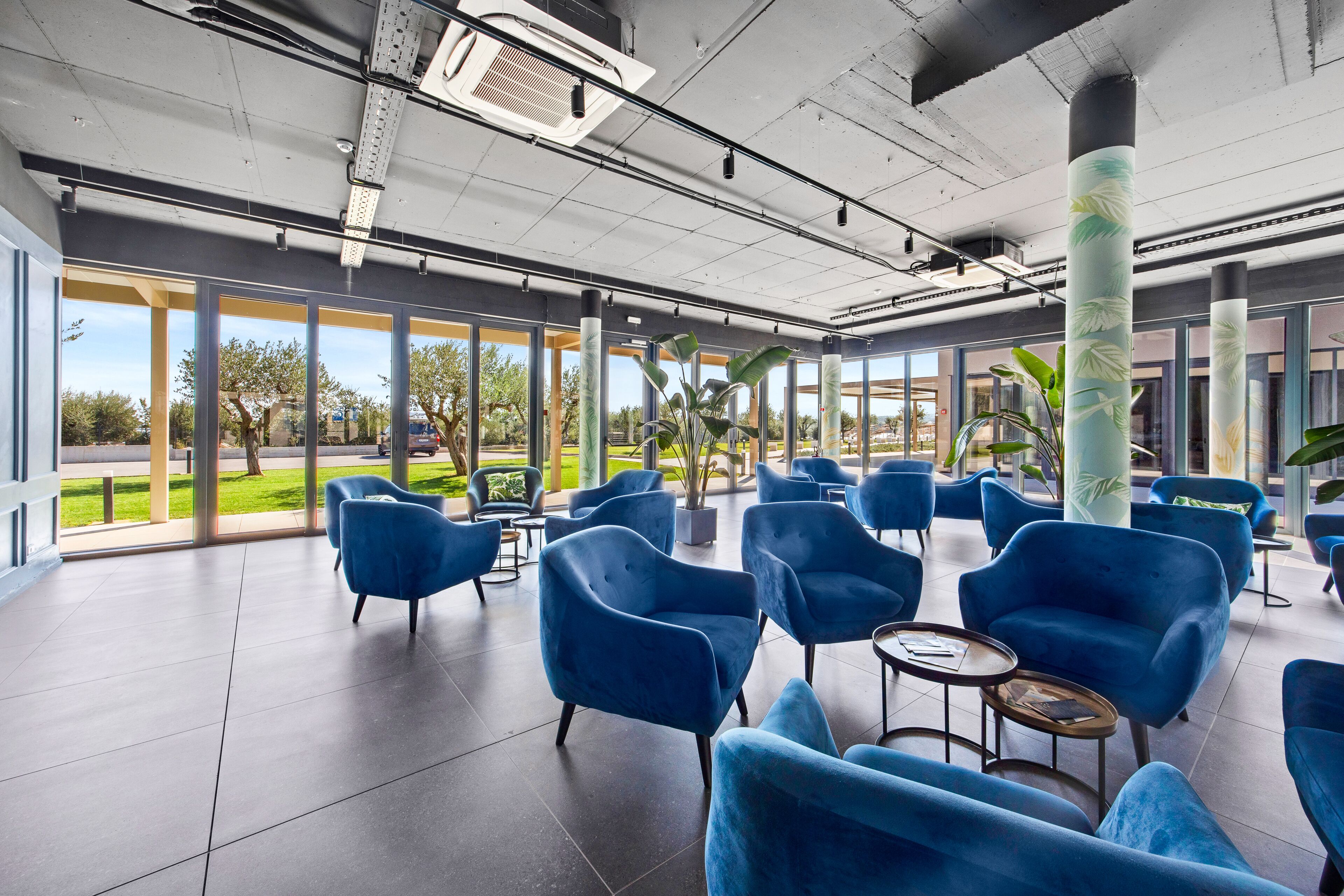 A spacious indoor area with blue chairs and tables, large windows offering views of greenery and a building outside.
