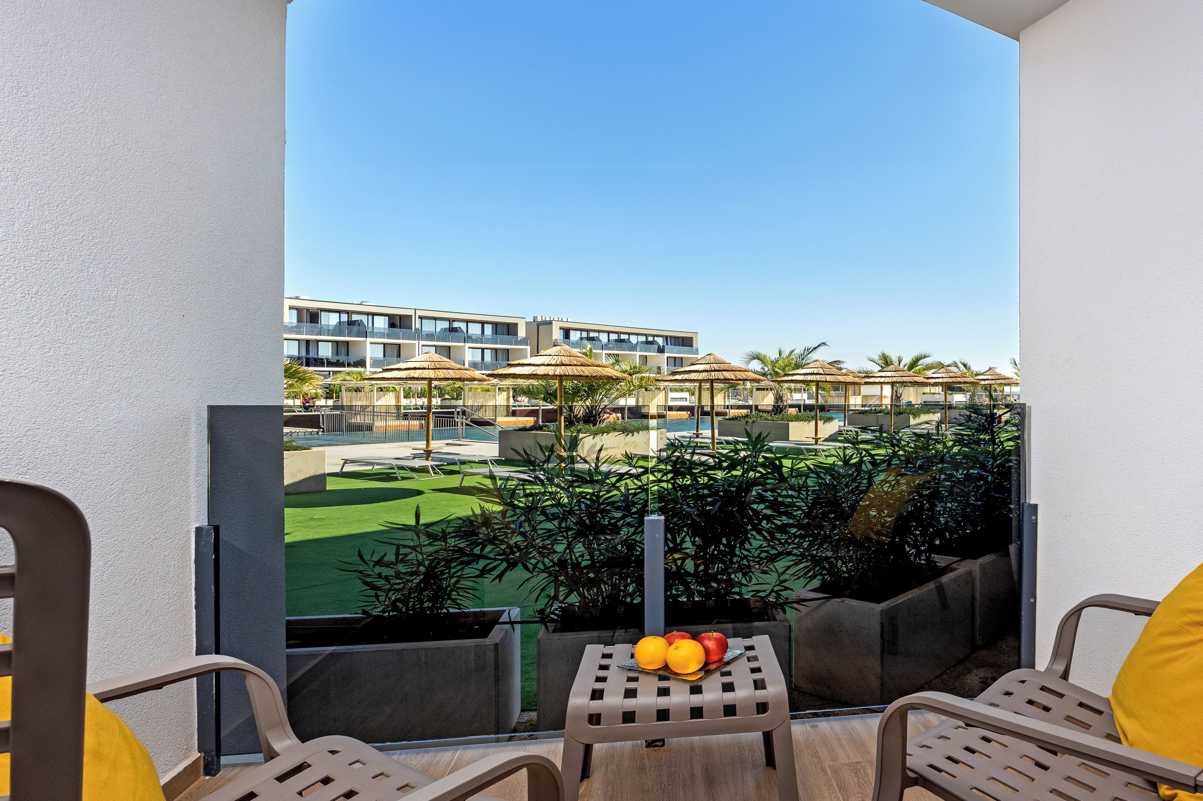 A balcony with a view of a pool, lounge chairs, and a table with fruit.
