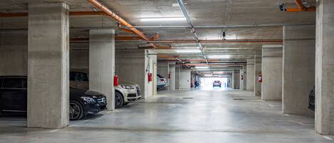 Un parking à plusieurs niveaux, avec des piliers en béton, des tuyaux apparents et des extincteurs.