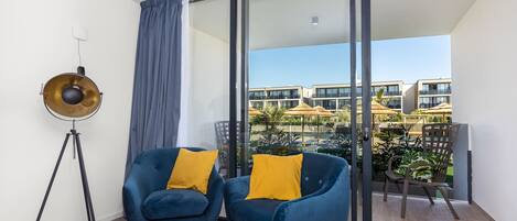 Un balcon avec deux fauteuils bleus et un lampadaire, donnant sur un espace piscine agrémenté de parasols.