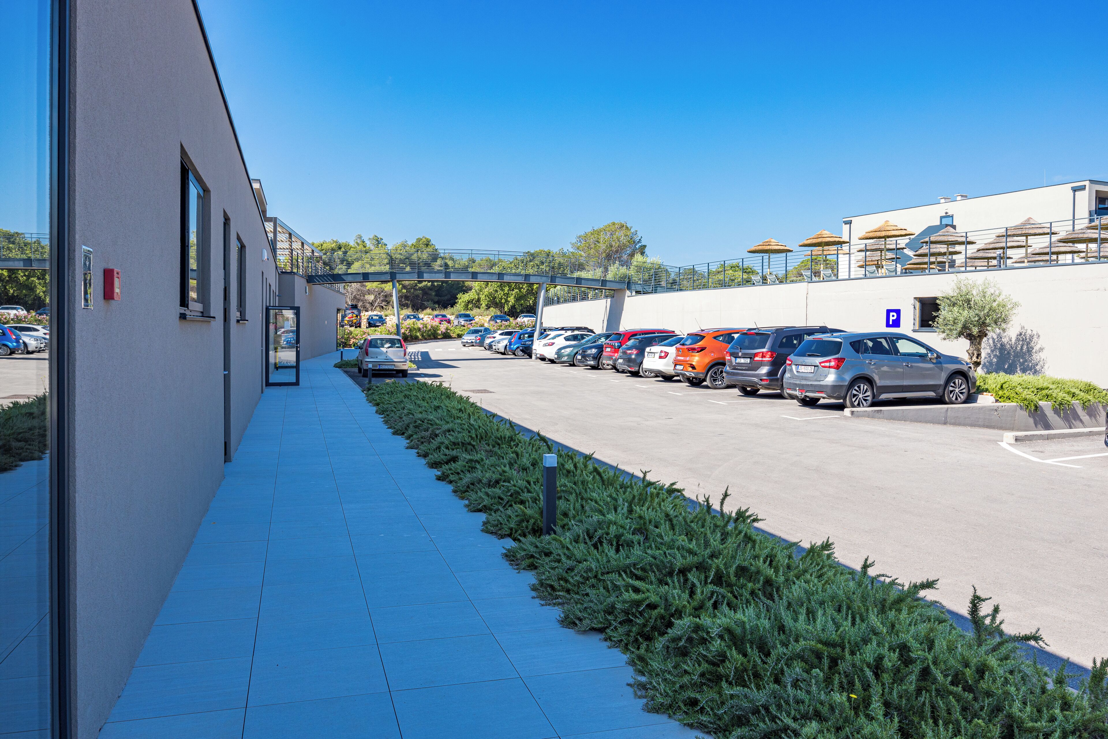 A parking lot with multiple cars and a building with a blue-tiled walkway.
