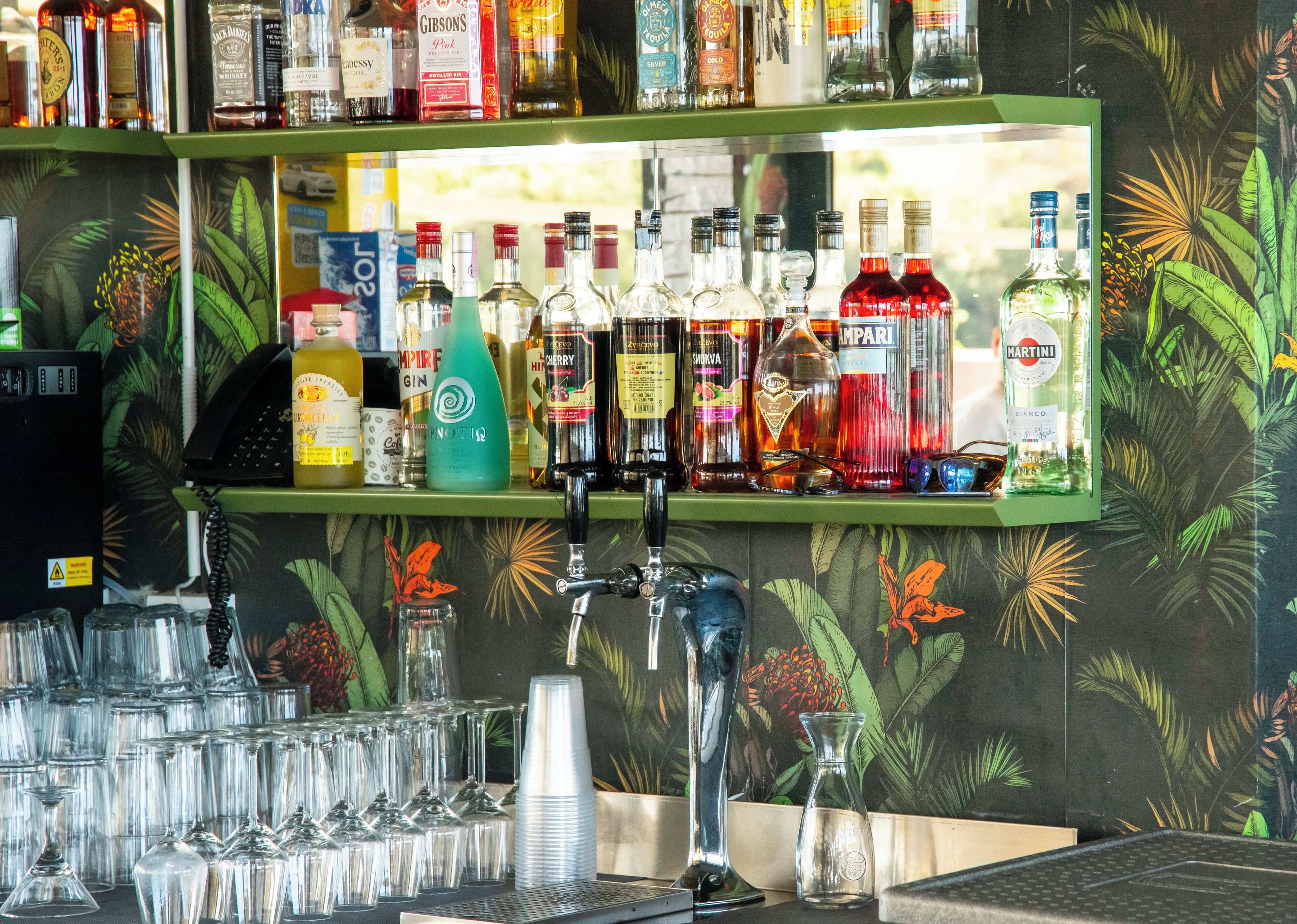 A bar area with shelves stocked with various liquor bottles, glasses, and a cash register.