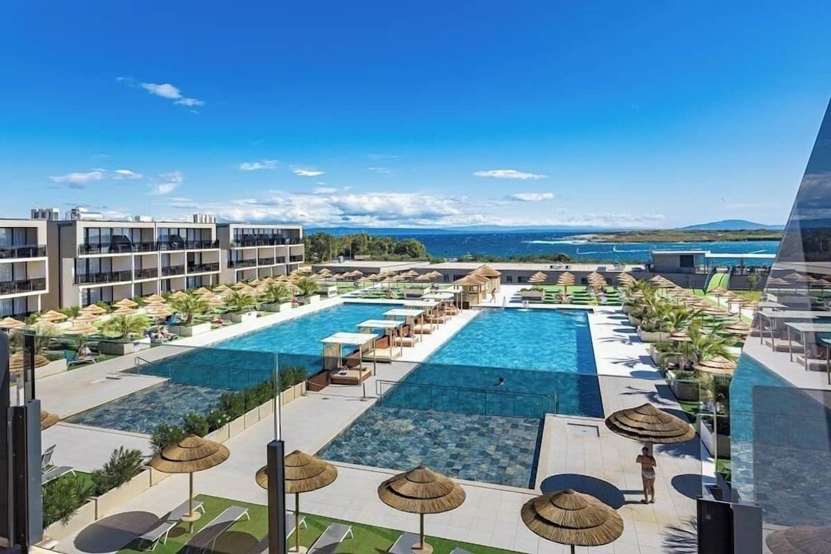A resort with multiple swimming pools, lounge areas, and a view of the sea.