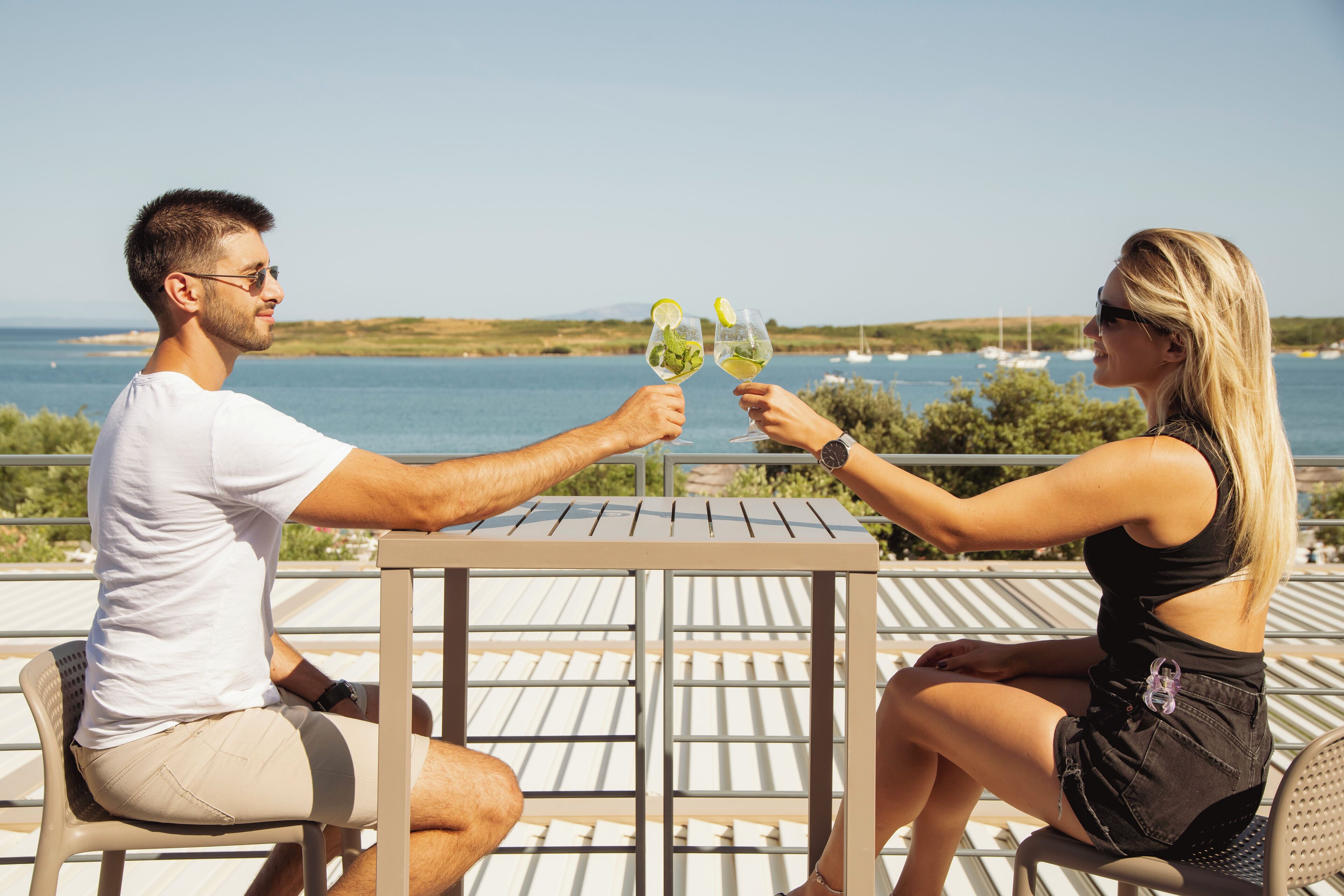 Two people sitting at a table with a view of the sea and boats in the background.