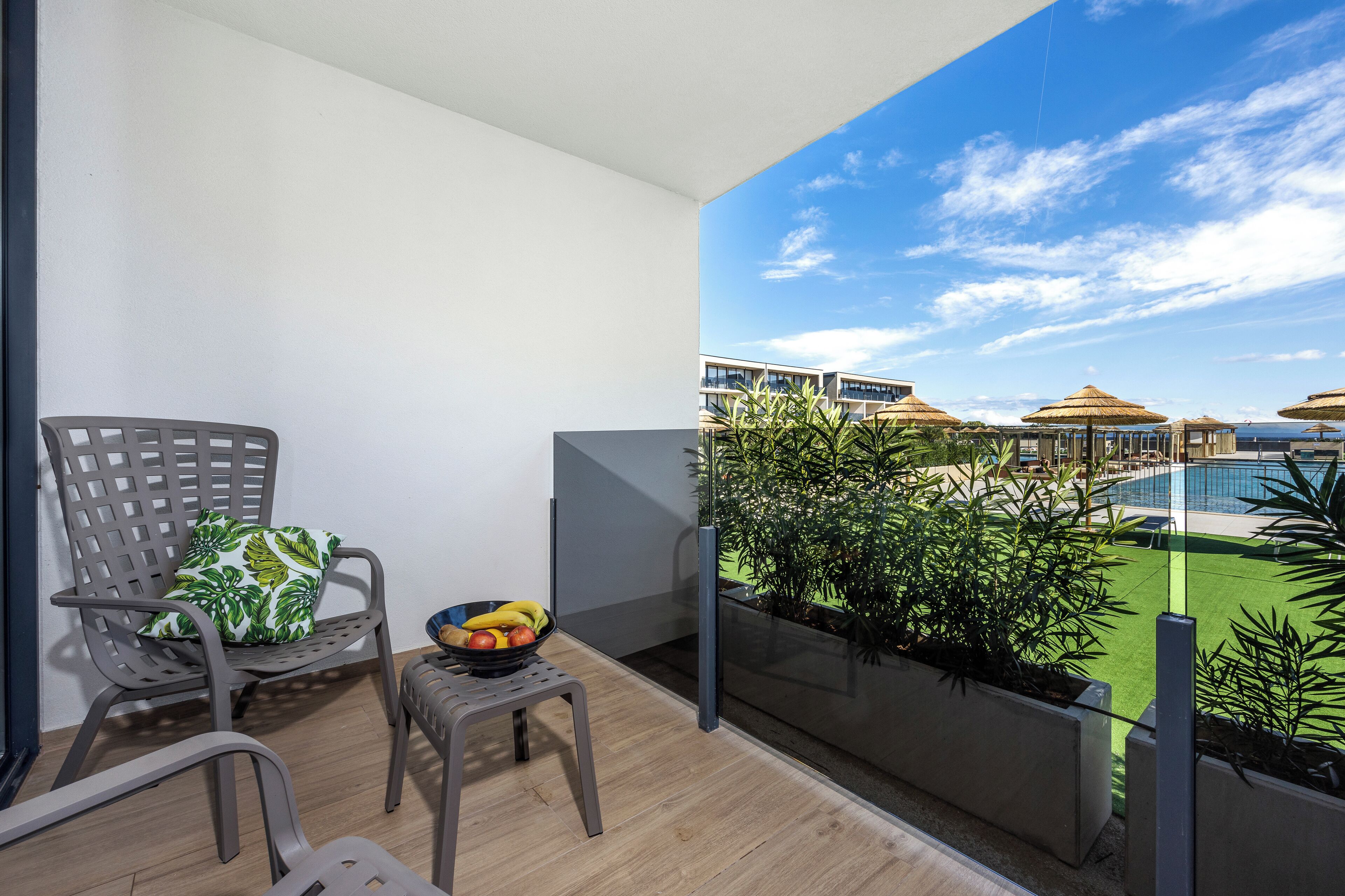 A balcony with a chair, a small table, and a bowl of fruit.