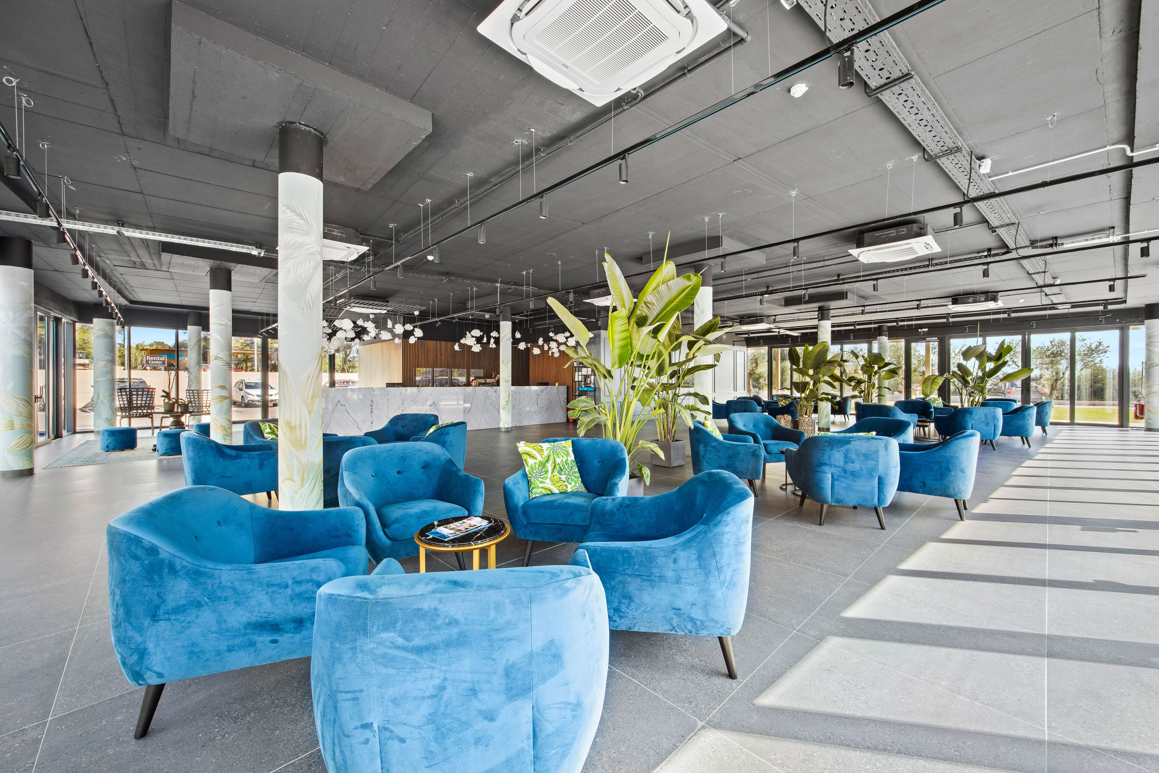 A spacious indoor area with blue upholstered chairs arranged around tables, large pillars, and potted plants.